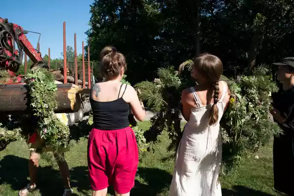 Women around a mast, making the pine wreath-like decoration for the structure.