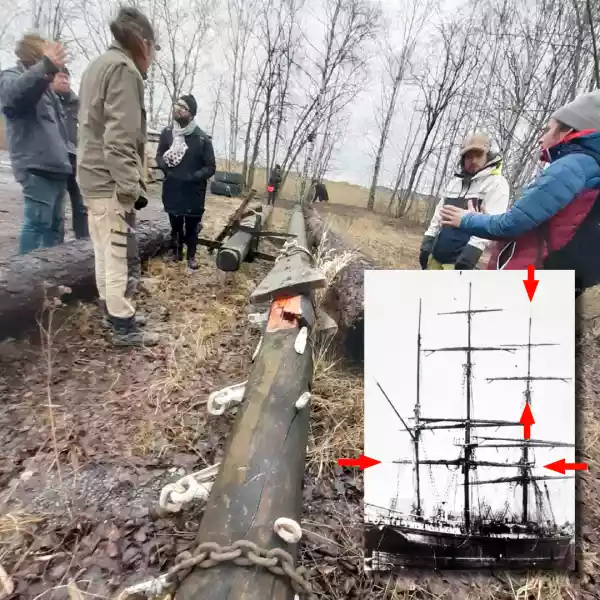 Image of peopel discussing around a large mast on the ground in a shipyard with an image of the original ship from which the mast came from.