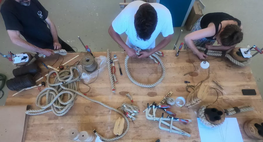 Image of people around a wooden table making deadeyes together.