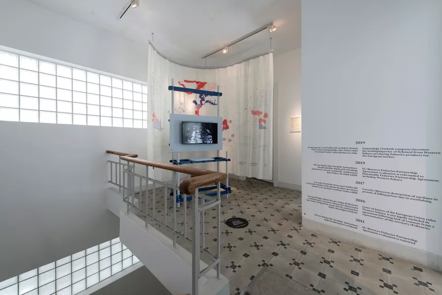 Installation overview of the 'Partnerships' work by FRAUD in 2020 at the Istanbul Design Biennial, showing curtain, video and print objects.